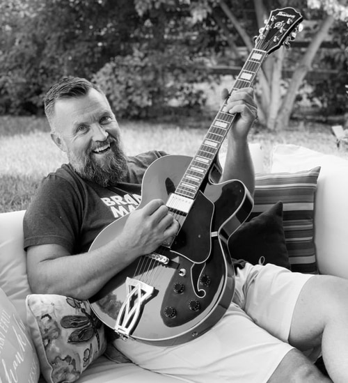 CEO Shane George sitting on a bench playing a guitar