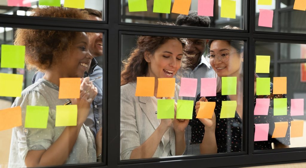 A group of business professionals in a brainstorming session writing on post-it notes on windows.