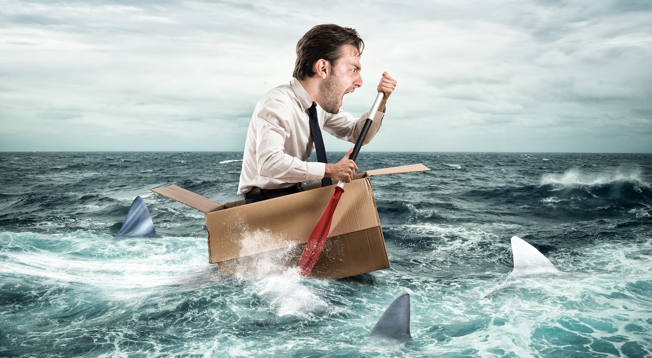 businessman in troubled waters yelling and trying to paddle his way out of sharks who surround him